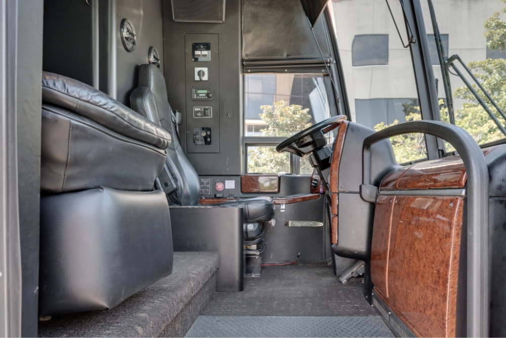 Driver's area and front seating of a Prevost H345 bus conversion for sale, highlighting the comfortable driver’s cockpit and premium leather seating, perfect for entertainer bus journeys.
