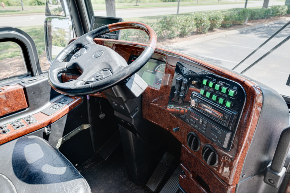 Close-up of the steering wheel and dashboard controls in a Prevost H345 bus, highlighting the detailed control panel and luxurious wood finish.