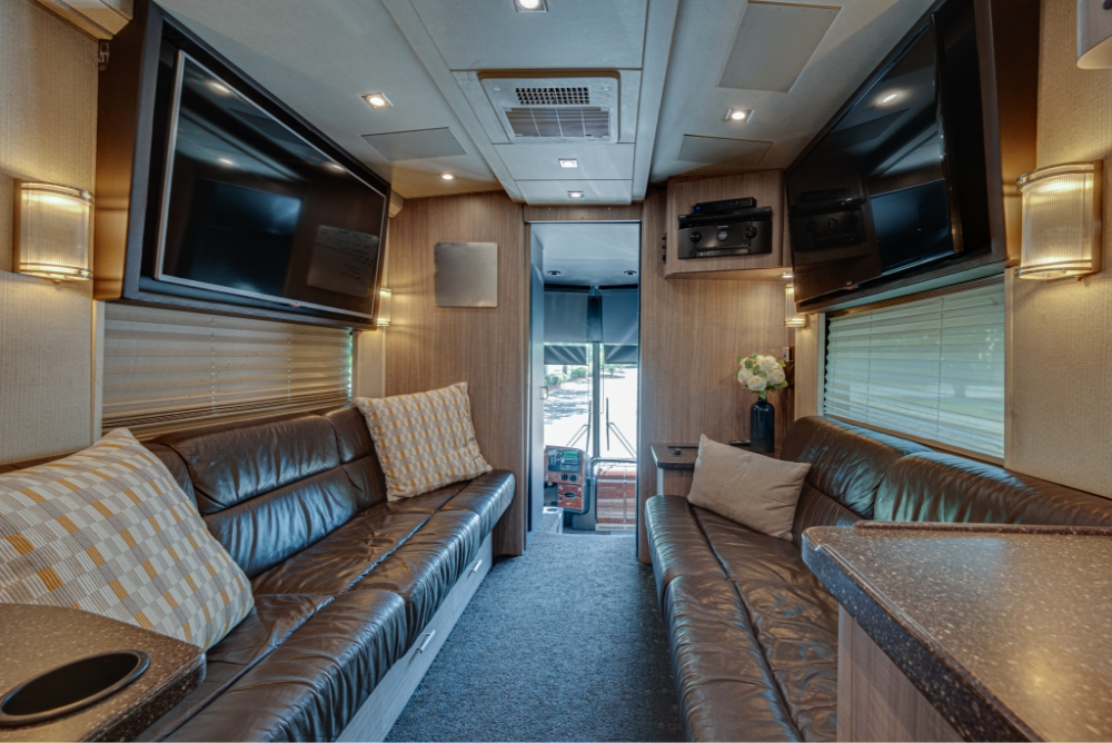 Spacious interior lounge of a Prevost H345 bus, featuring comfortable leather seating and flat-screen TV for luxury travel and entertainment.