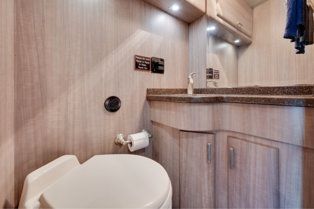 Bathroom area in a Prevost H345 bus conversion, showing the sink and toilet setup with modern design and functionality for on-the-go convenience.