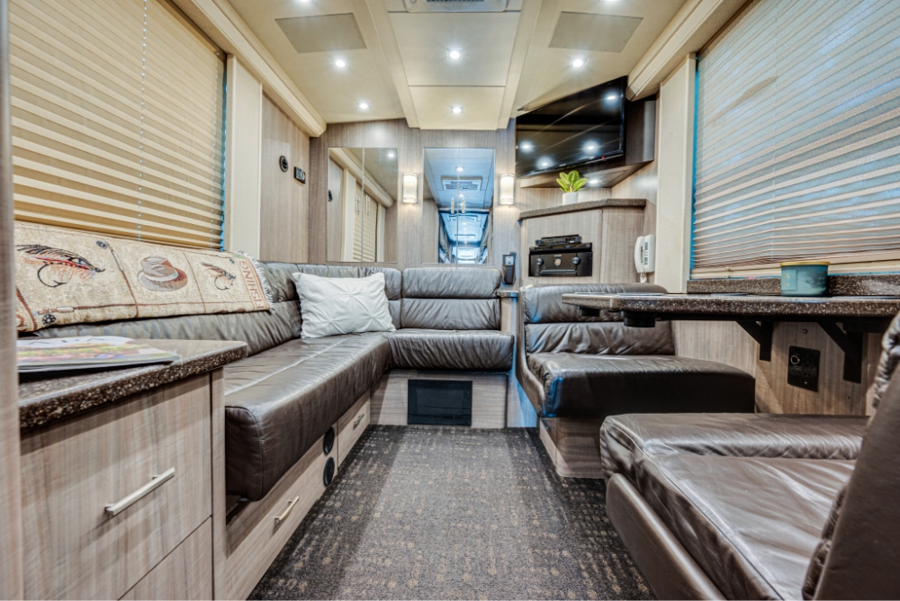 Wide-angle view of the lounge area in a Prevost H345 bus conversion, featuring a large sectional leather couch for comfortable relaxation during travel.