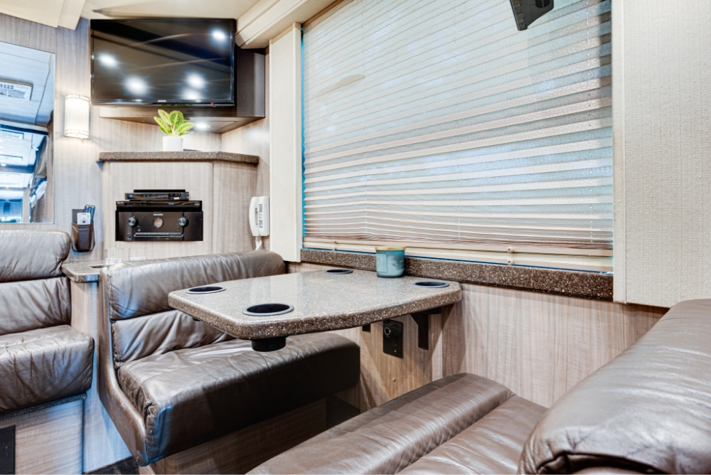 Lounge area in a Prevost H345 bus, showing a leather couch and entertainment setup with a flat-screen TV for luxury travel accommodations.