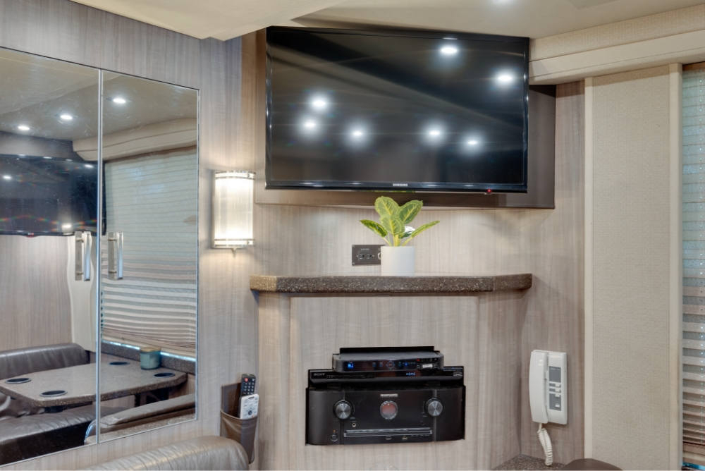Entertainment center in a Prevost H345 bus, featuring a mounted flat-screen TV and shelving, perfect for entertainment on the road.