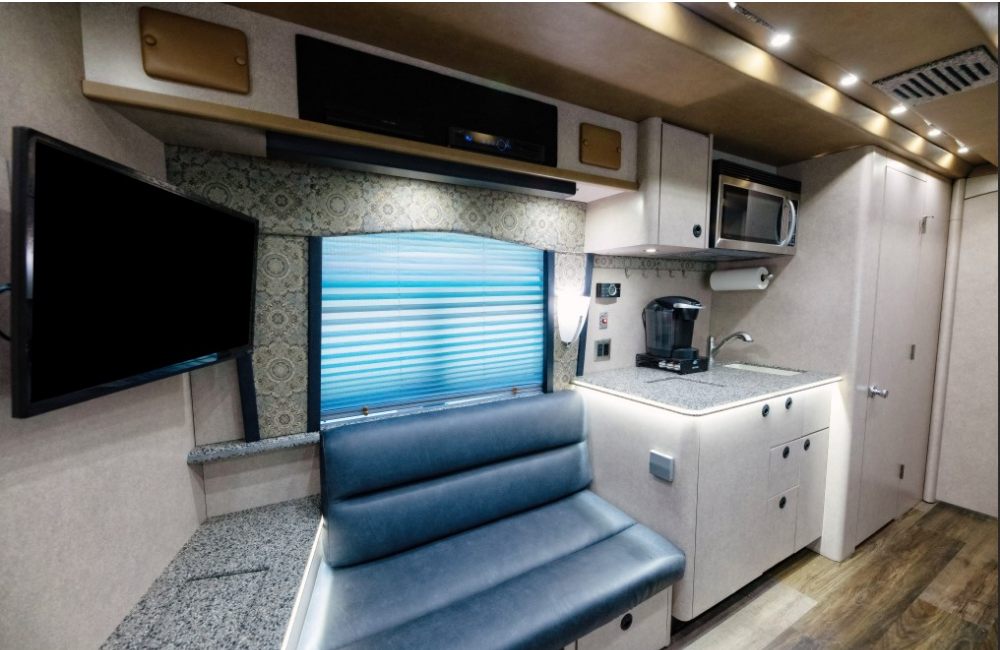 Close-up of the dining and kitchen area inside the 2007 Prevost XLII, showcasing booth seating, a mounted TV, and kitchen amenities