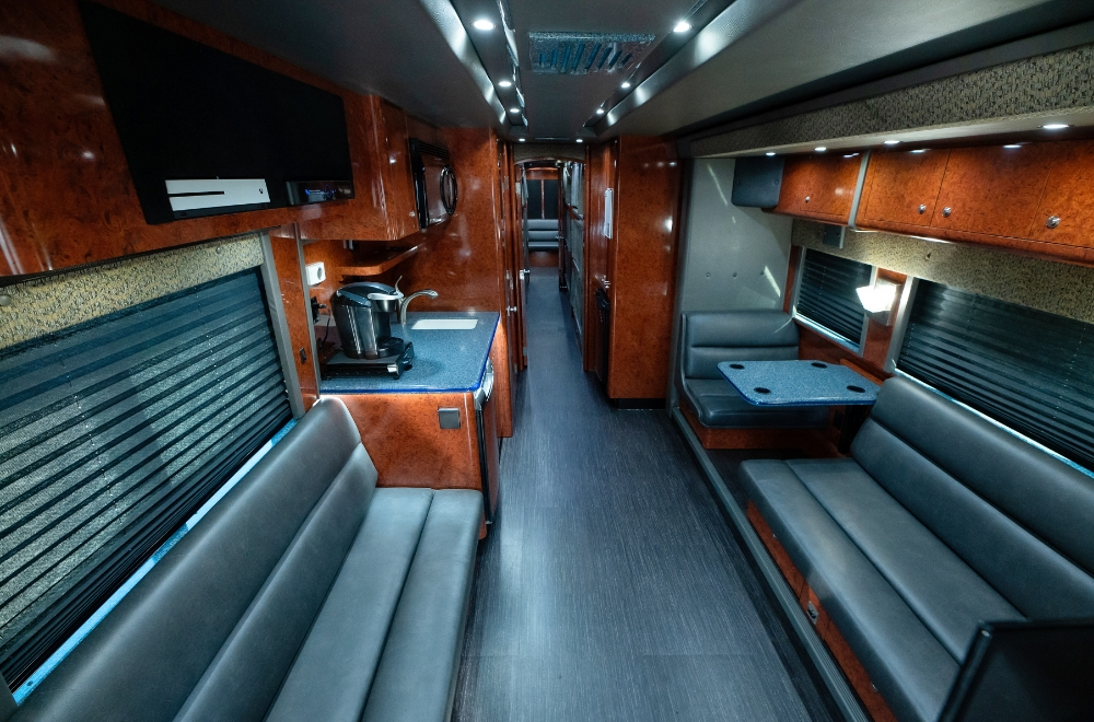 Spacious living area inside a Prevost bus conversion showcasing multiple leather seating options and custom wood cabinetry, making it a perfect mobile office or entertainer space.