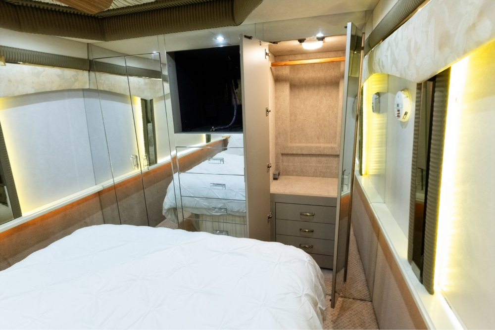 Private bedroom in a 2000 Prevost H345 bus conversion for sale, featuring a comfortable bed, TV, and ample storage, perfect for long-distance motorhome travel.