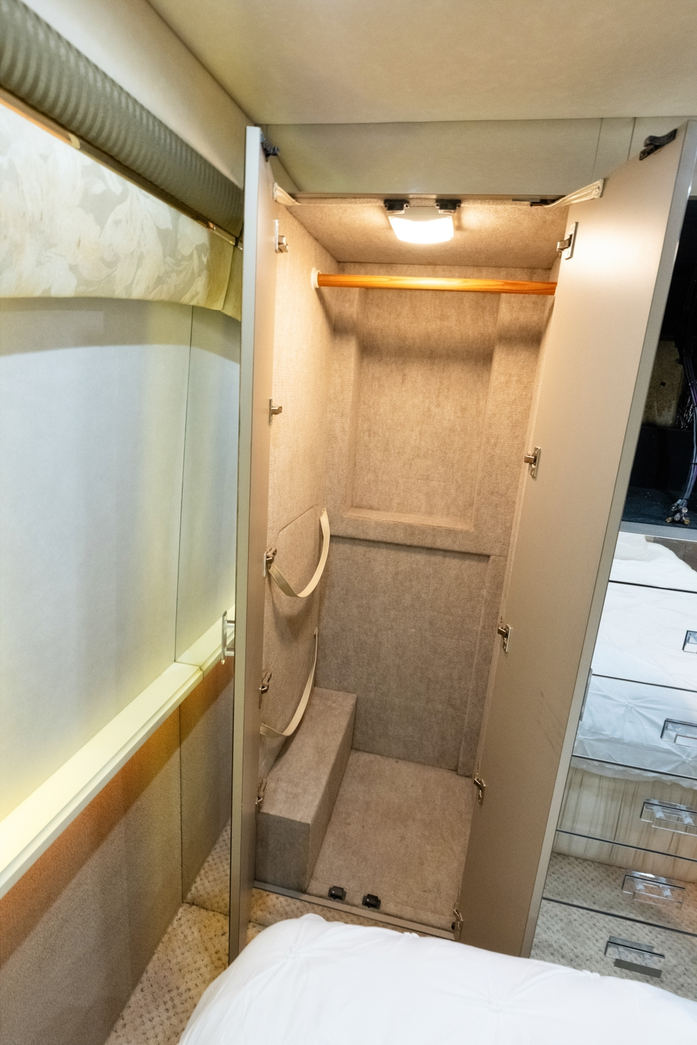 Storage closet inside a 2000 Prevost H345 bus conversion for sale, featuring built-in lighting and ample space for storing personal items, with soft interior finishes.