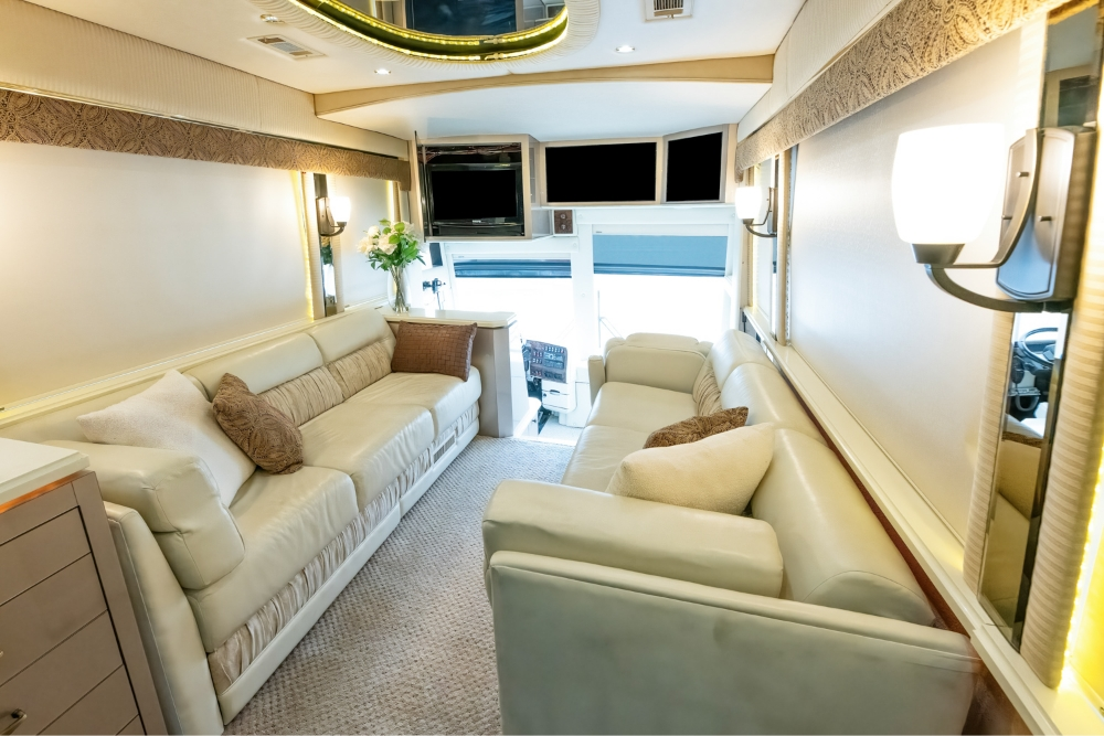 Front lounge area of a 2000 Prevost H345 motorhome for sale, showcasing comfortable white leather sofas and a TV for relaxation and entertainment.