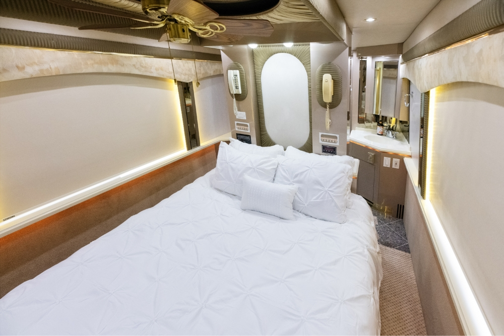 Master bedroom in a 2000 Prevost H345 motorhome for sale, showcasing a large, comfortable bed and sleek modern lighting for a luxury travel experience.