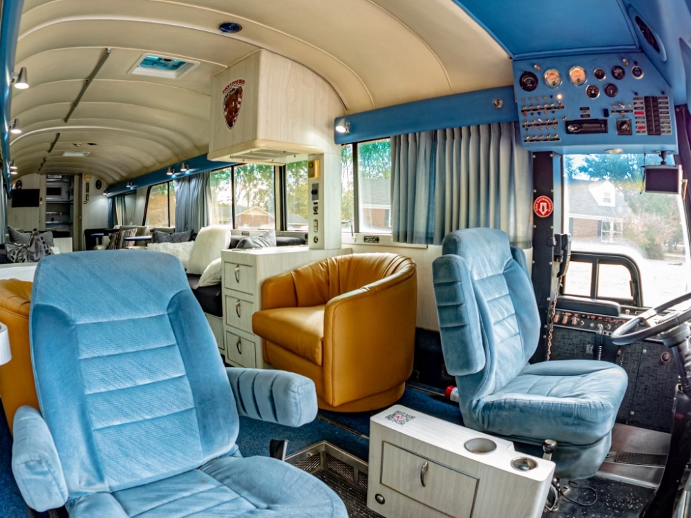 Driver's cockpit and front lounge seating inside a 1976 MCI 8 Custom Coach, providing a spacious and well-maintained driver area for long trips.