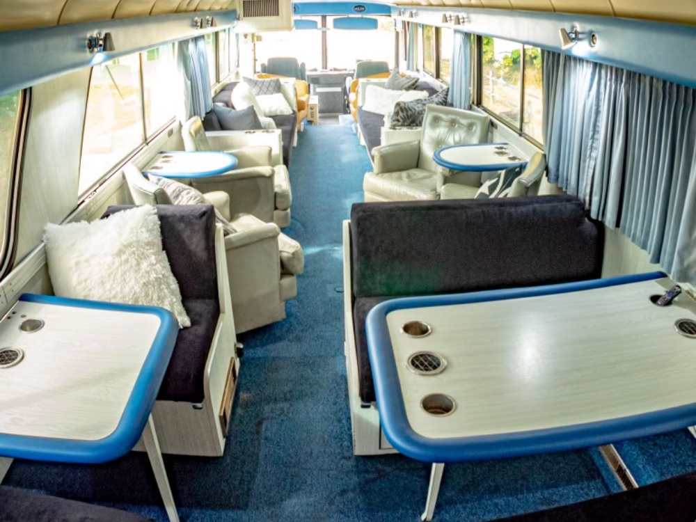 Spacious dining and lounge area inside a 1976 MCI 8 bus conversion for sale, featuring tables and sofas, perfect for executive meetings or relaxation during travel.