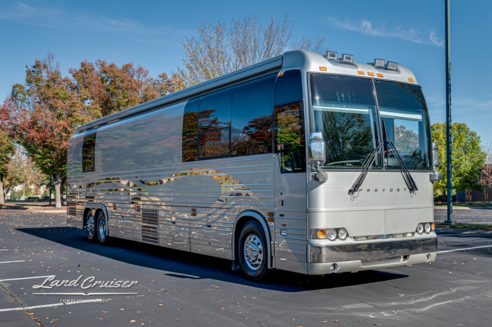 2006 Prevost XLII tour bus in silver, parked with trees in the background.