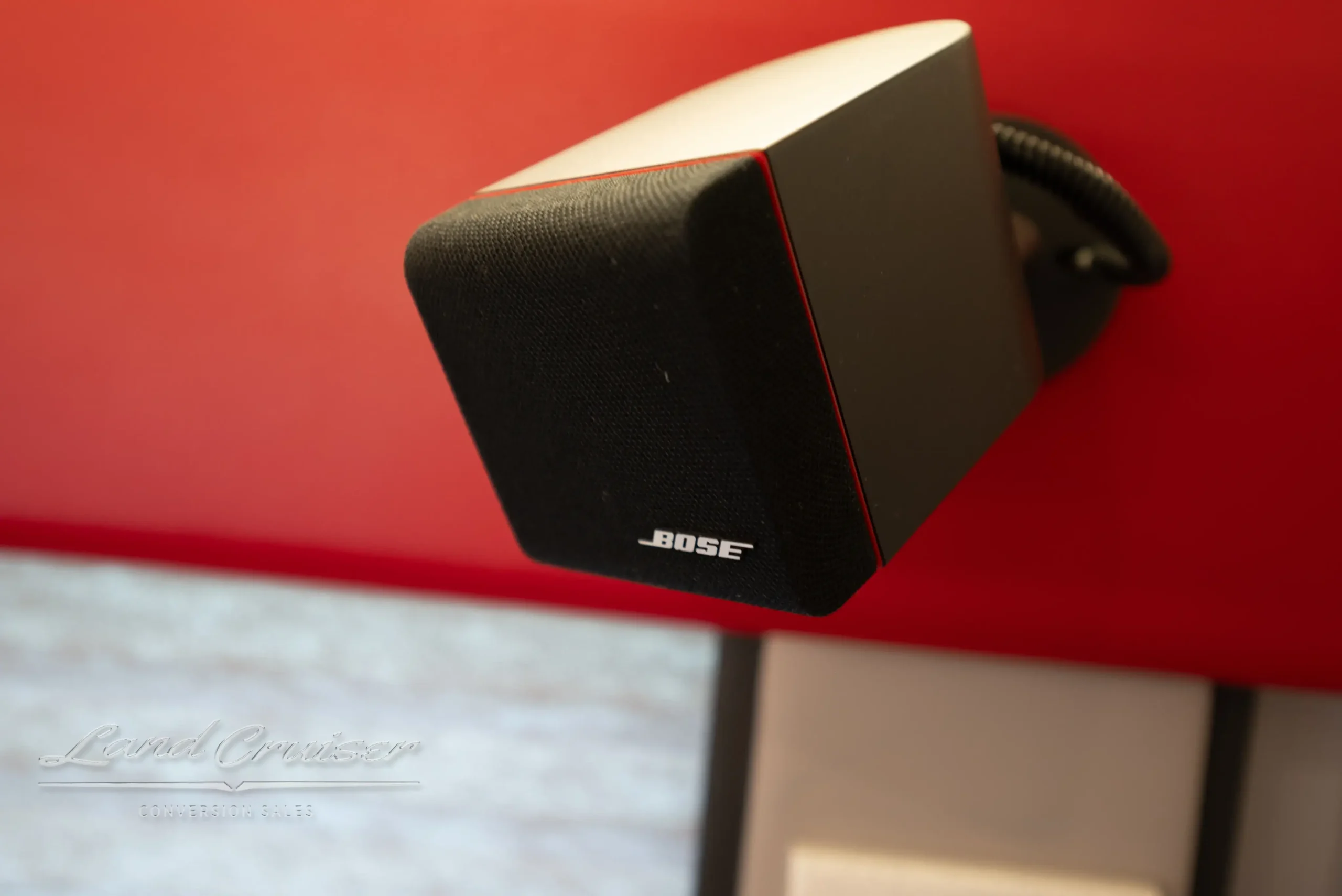 Bose surround speaker mounted in MCI executive coach interior near red leather wall