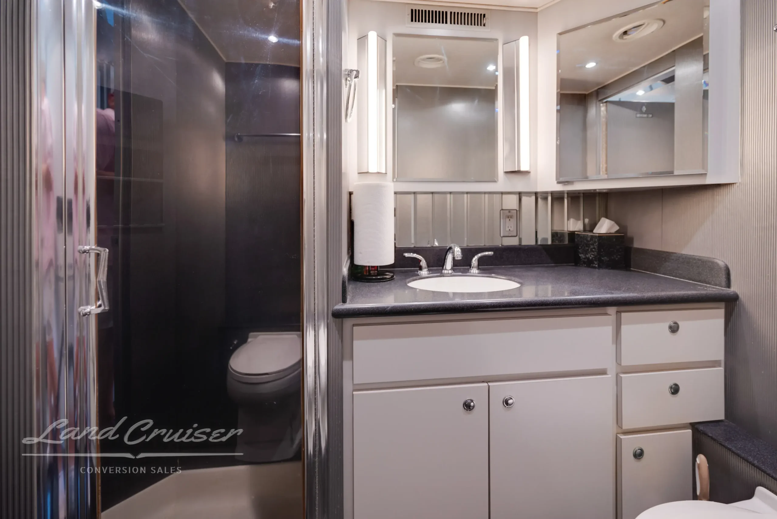 Modern bathroom in MCI bus conversion featuring black countertop, white cabinetry, and glass shower