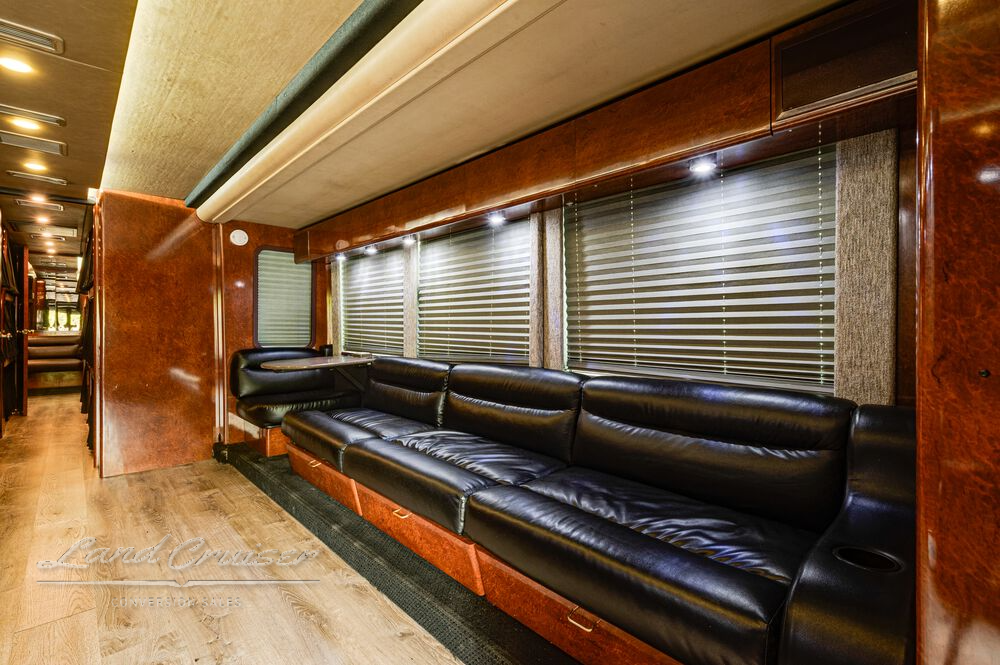 Passenger-side black leather couch in Prevost Shogun lounge with wood-paneled walls and blinds