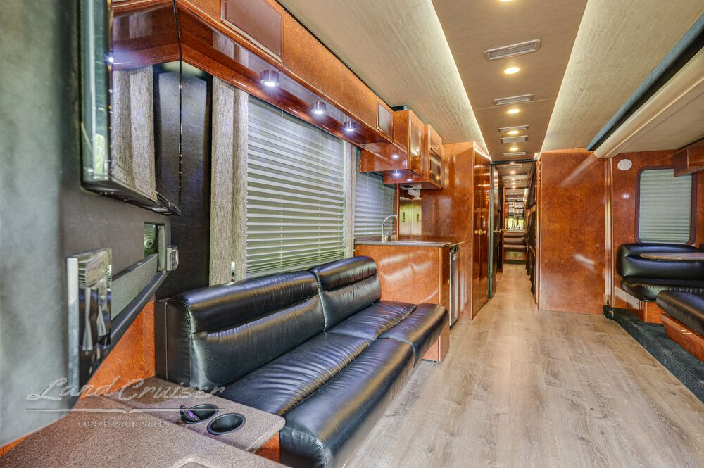 Driver-side view of Prevost coach lounge featuring black leather seating and overhead compartments