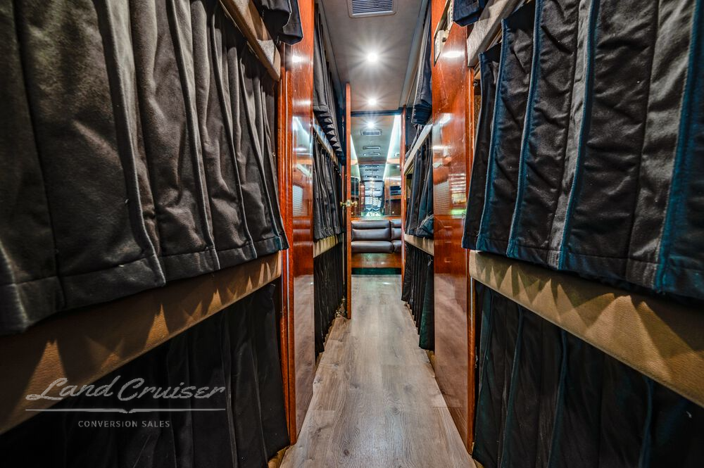 Hallway in Prevost 12-bunk entertainer coach with privacy curtains, hardwood flooring, and LED lights