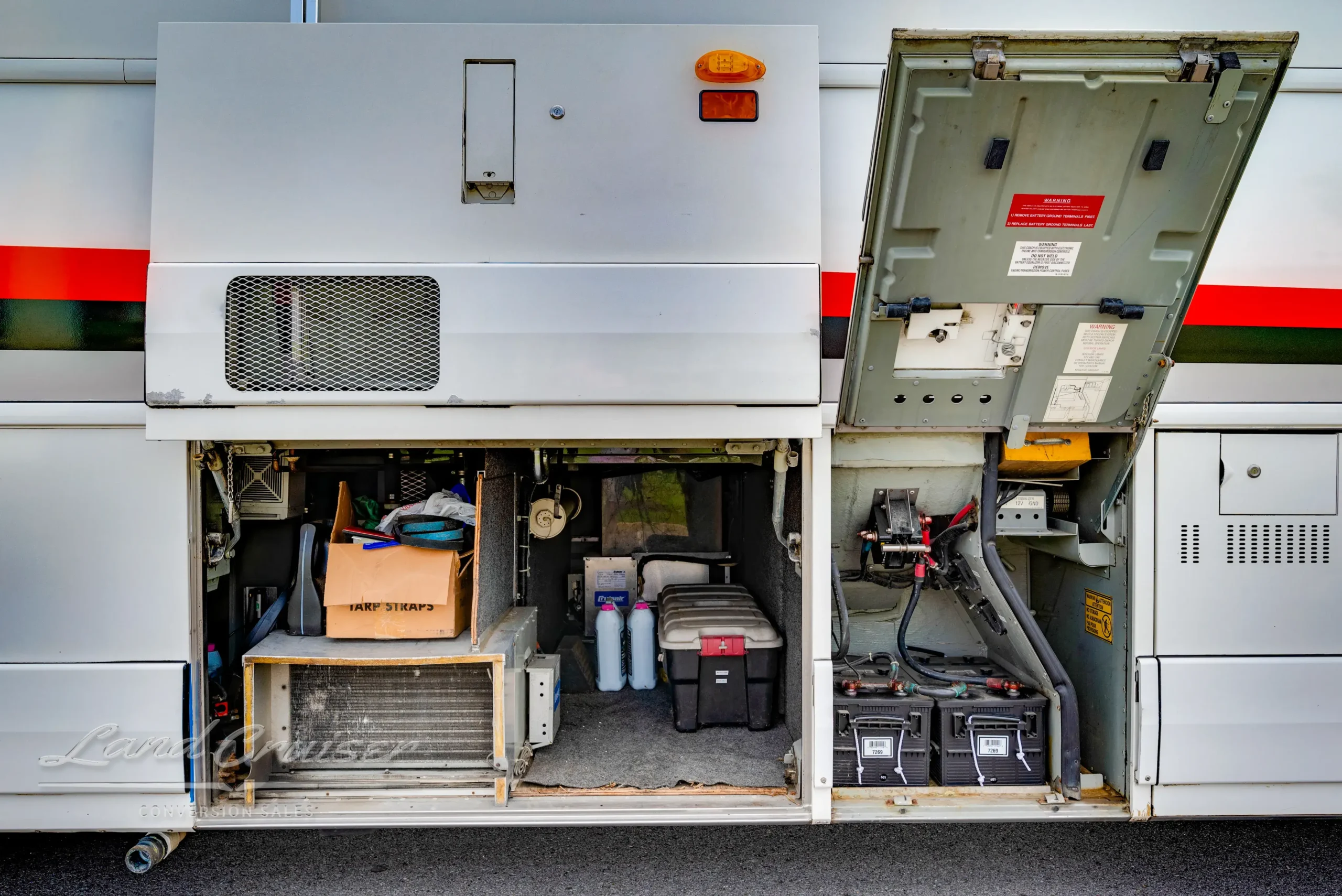 Open utility bays on MCI bus revealing generator, battery system, and undercarriage storage compartments