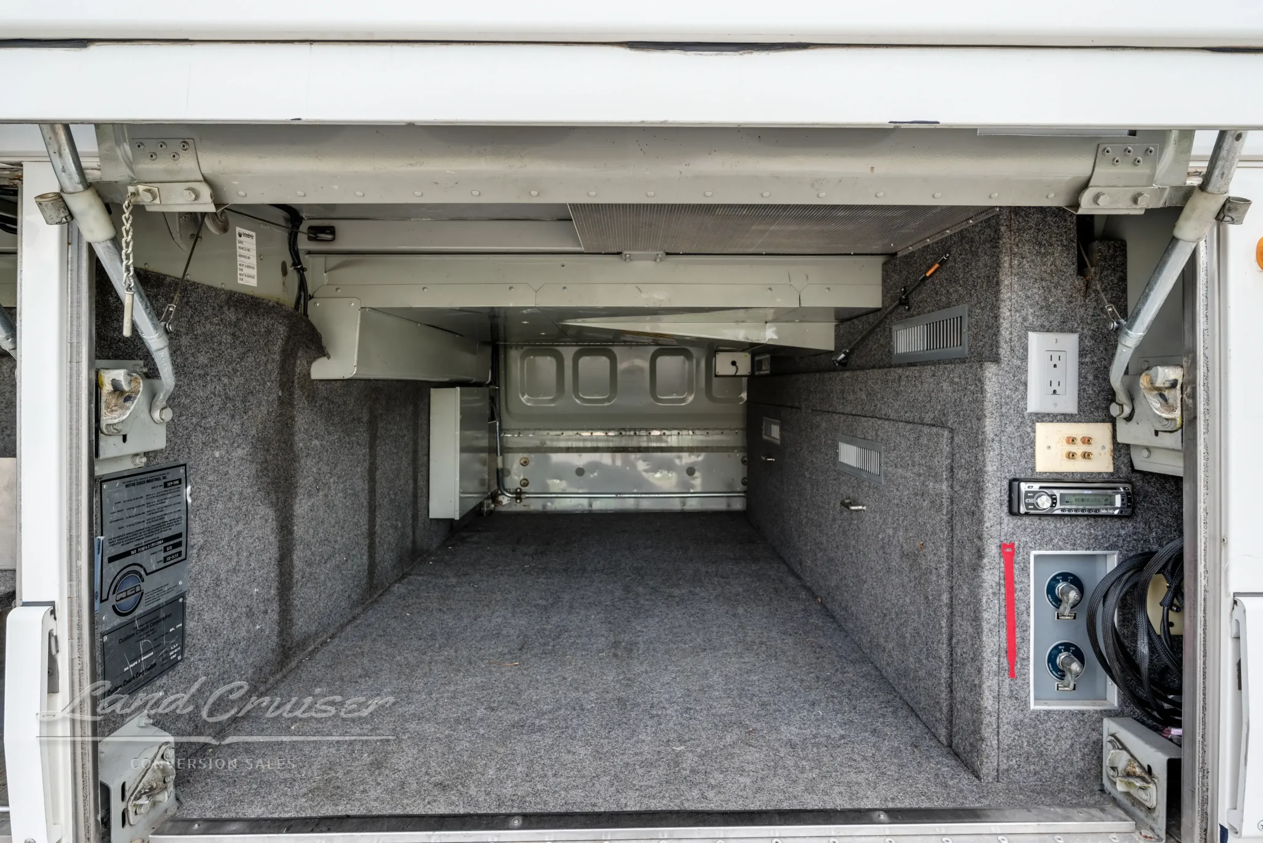 Interior view of undercarriage luggage bay in MCI bus conversion with carpeted walls and outlets