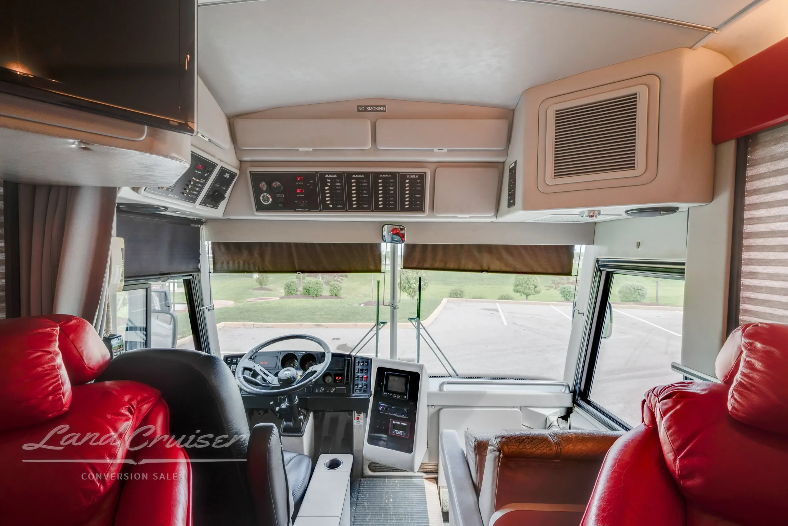 Driver area of MCI Executive Coach with Atlas II air ride seat, control panels, and red leather lounge chairs
