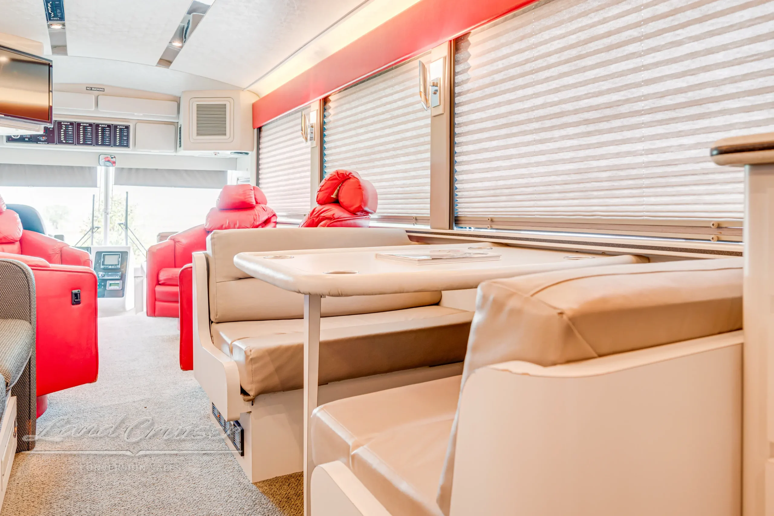 Booth-style dinette in MCI bus conversion with beige leather seating, red swivel chairs, and panoramic windows