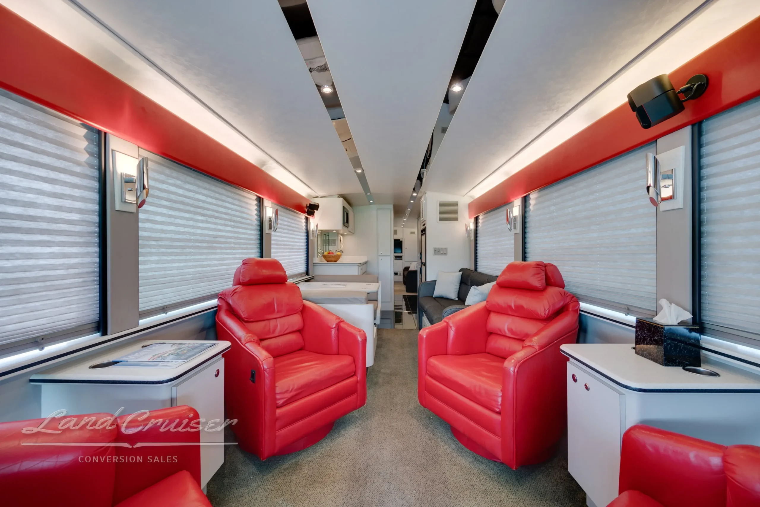 Executive rear lounge in MCI bus featuring four red swivel chairs, end tables, and accent lighting