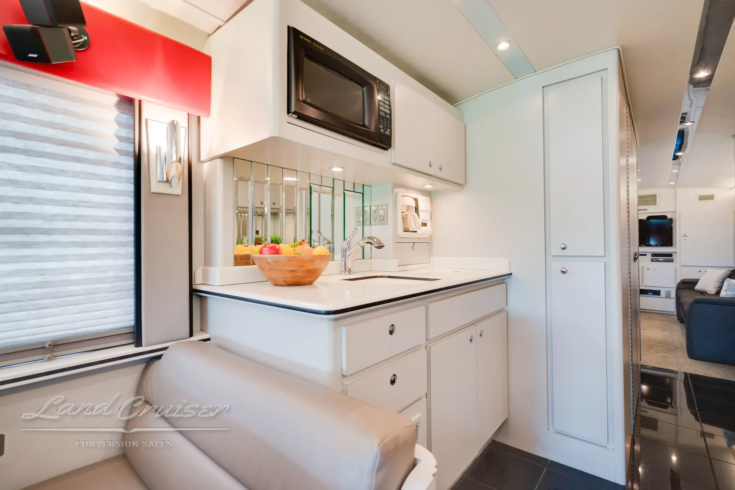 Kitchen galley in MCI 102-DL3 bus conversion featuring Sharp microwave, Corian counters, and mirrored backsplash