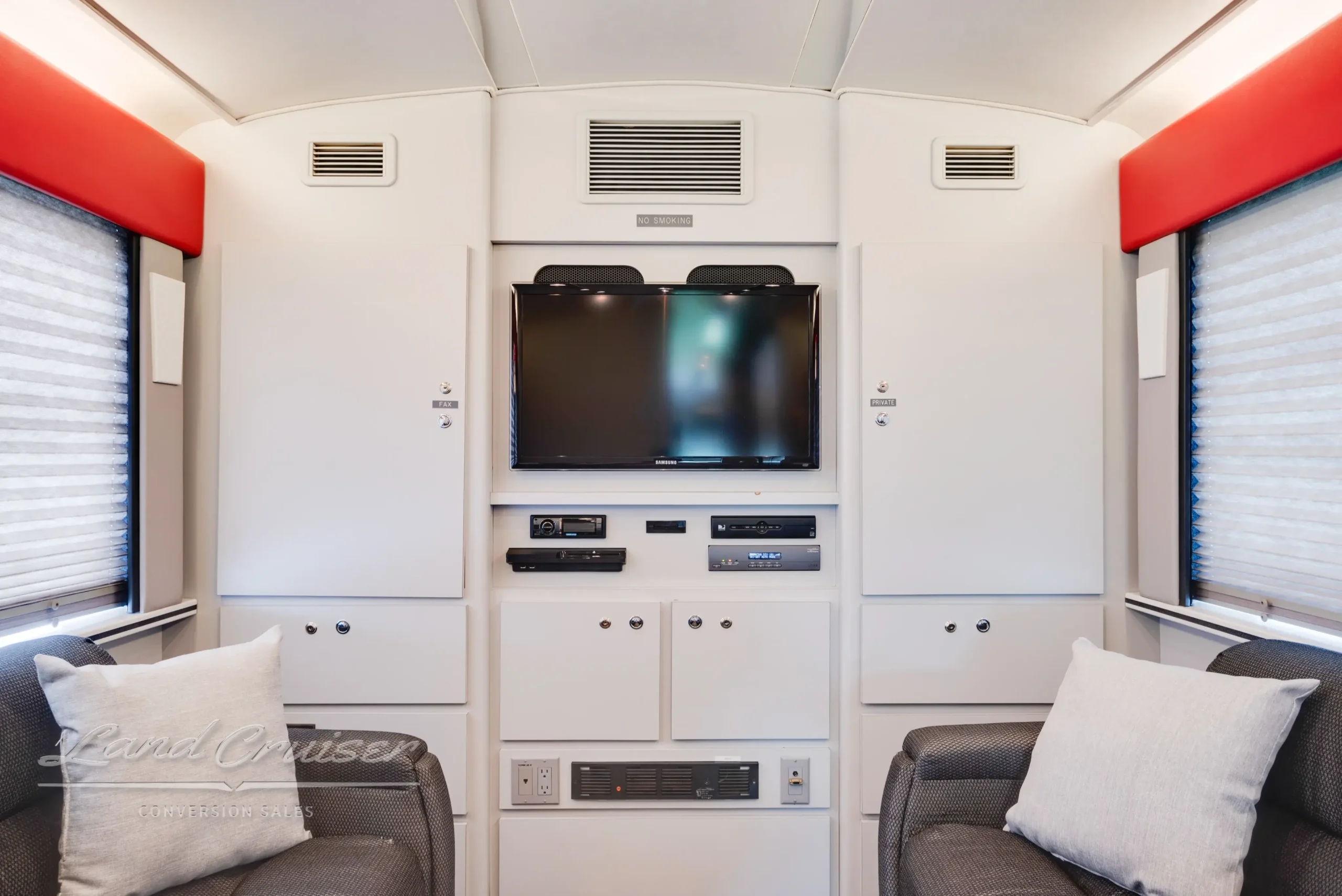 Rear lounge of MCI bus conversion featuring 32-inch Samsung TV, storage cabinetry, and Berber carpet