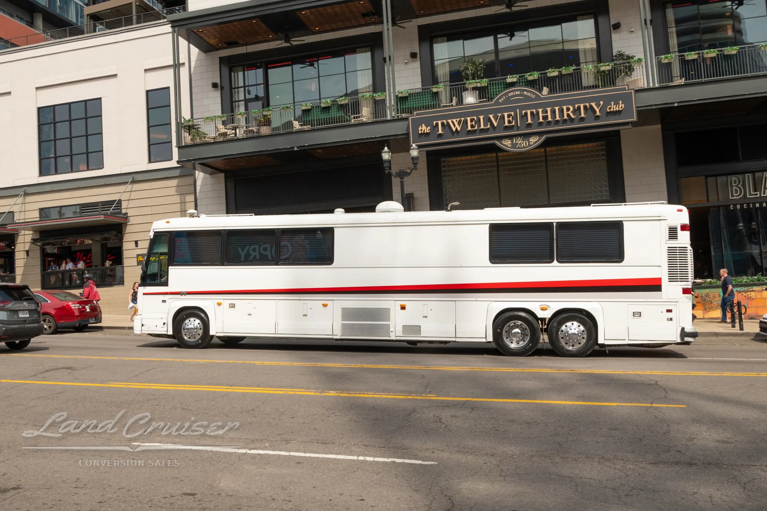MCI bus conversion parked in front of upscale retail and residential building in urban downtown setting