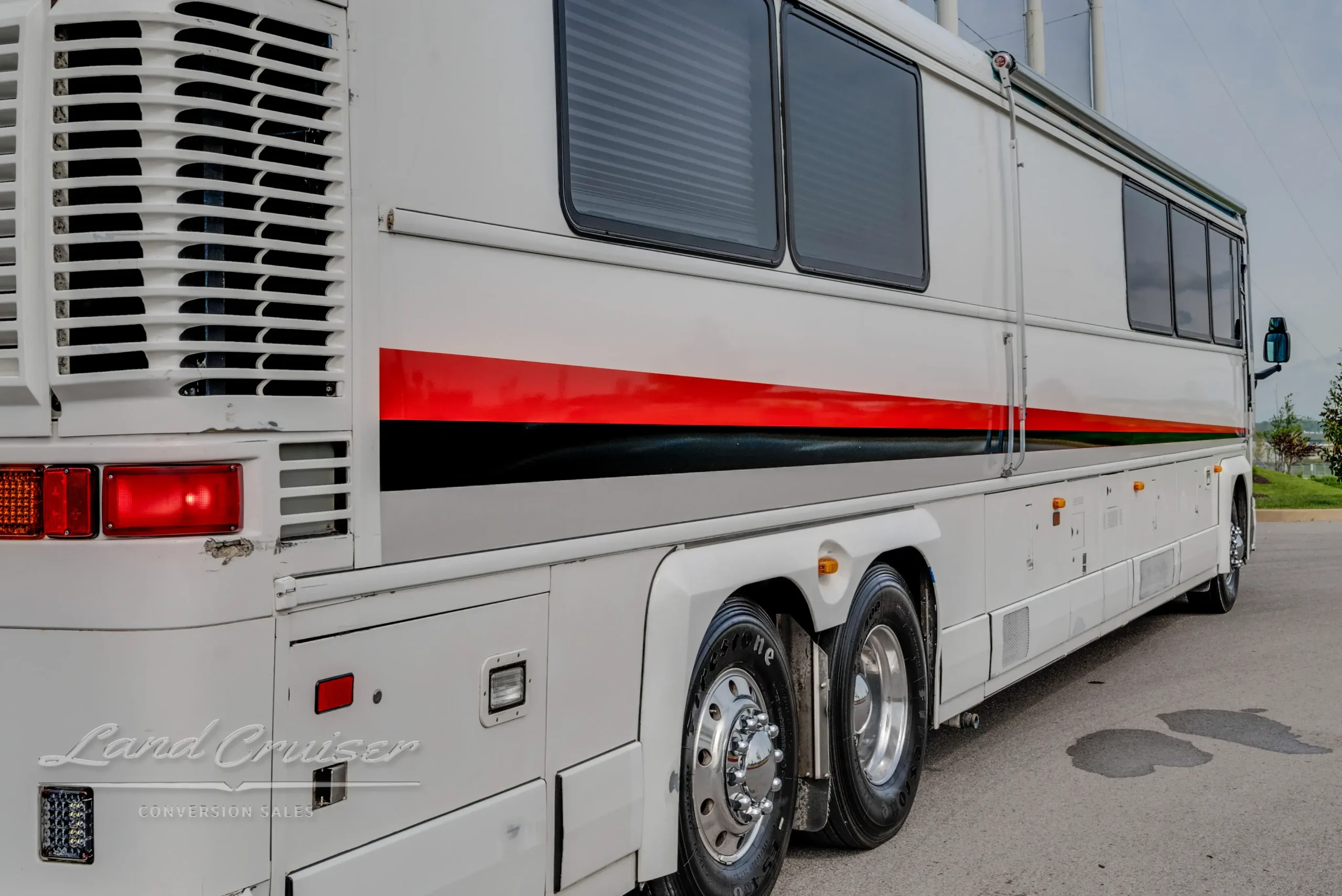 Passenger side of MCI 102-DL3 parked by netted athletic field, displaying red and black stripe