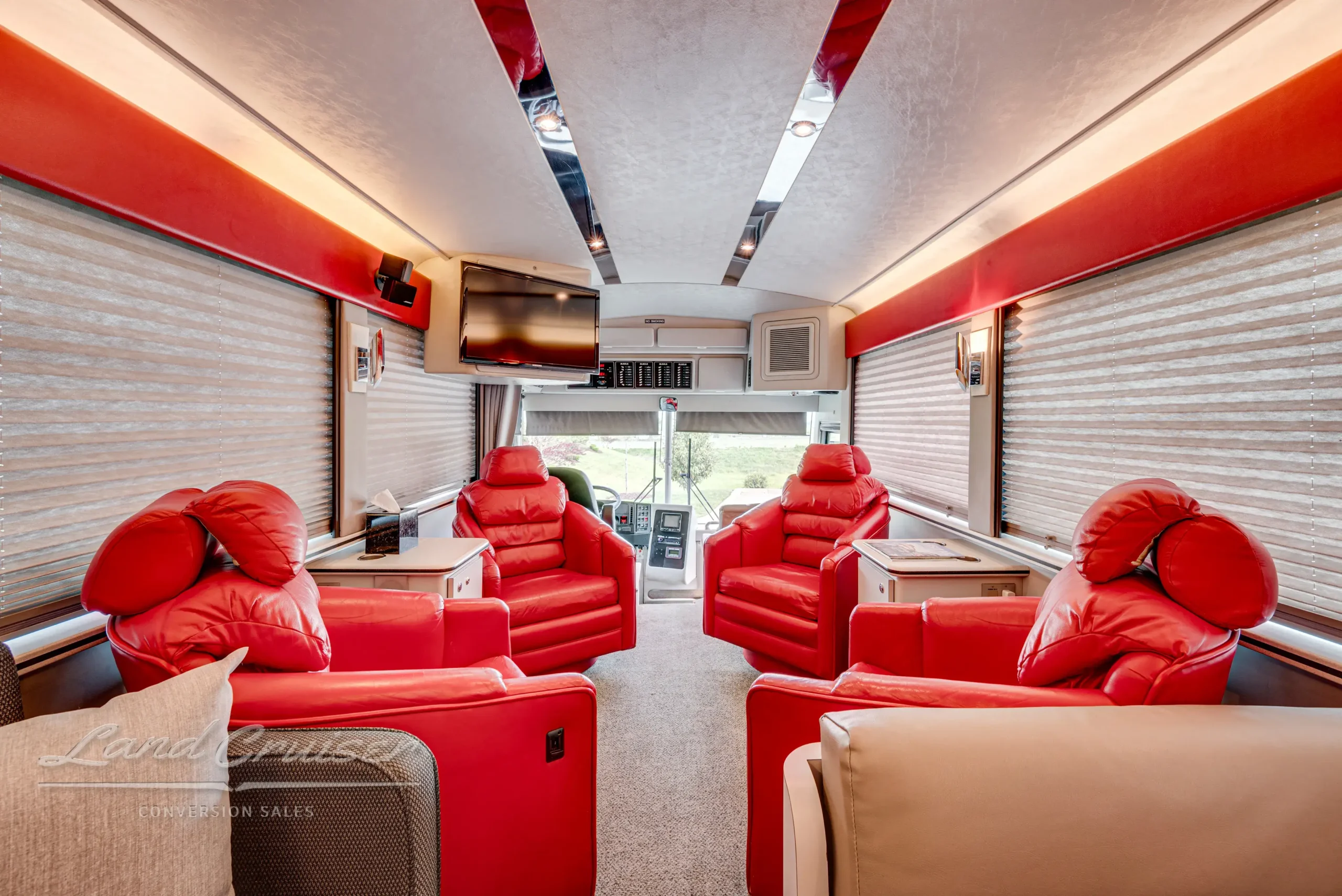 Main salon of MCI Executive Coach featuring four red swivel chairs, Berber carpet, and ambient lighting