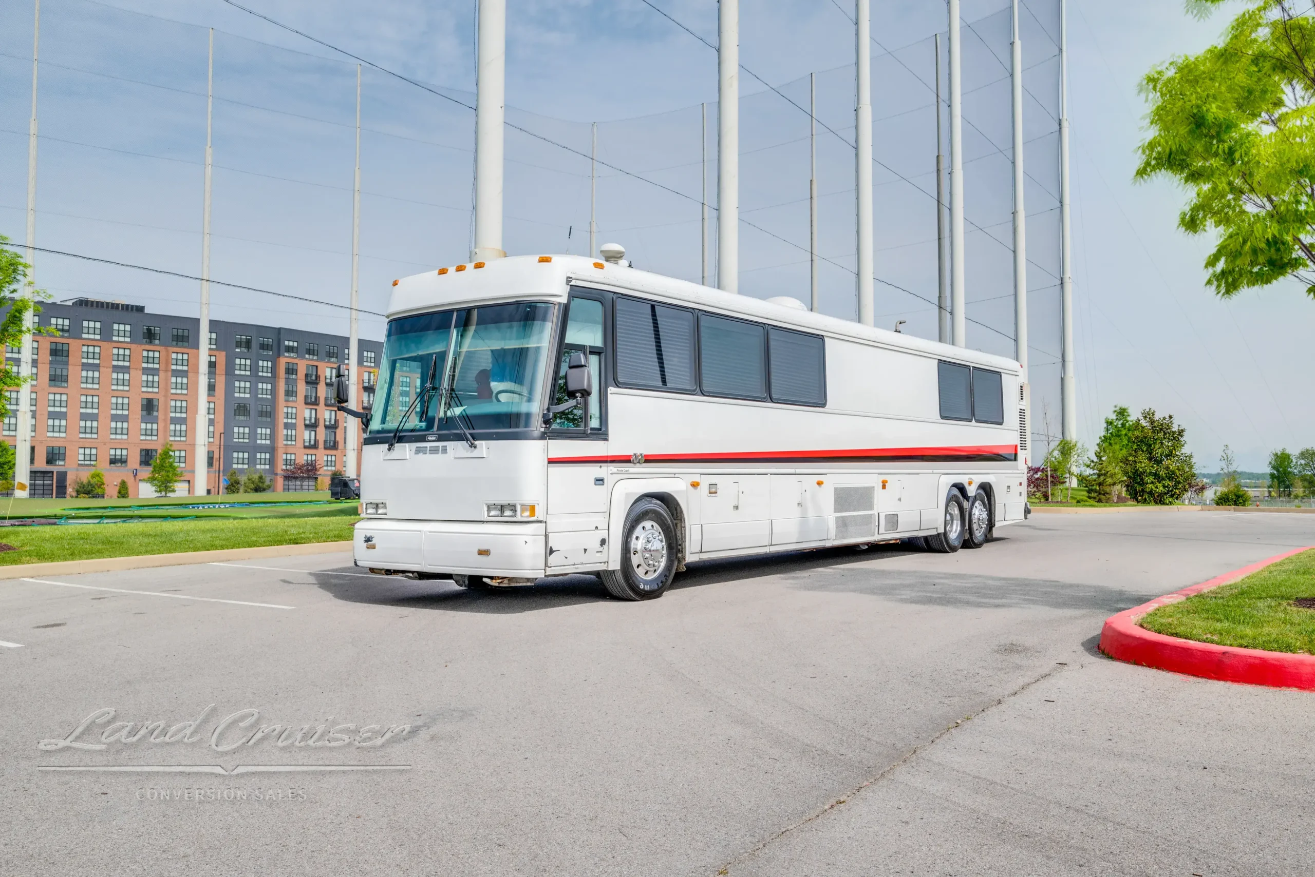 Full driver-side profile of MCI 102-DL3 bus parked outdoors with netted sports poles in background
