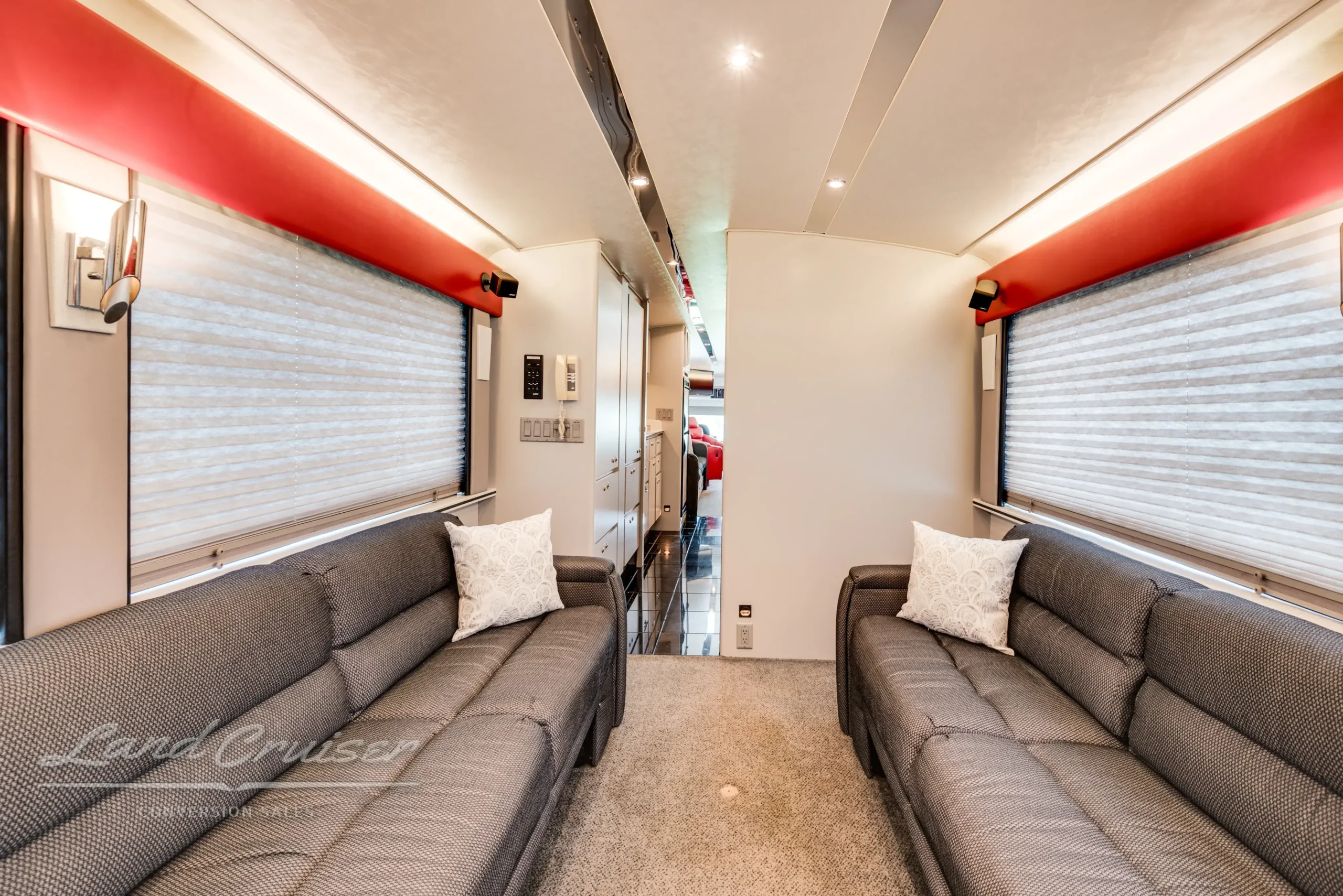 Side-facing gray lounge sofa in MCI bus conversion with wide windows, accent lighting, and neutral decor