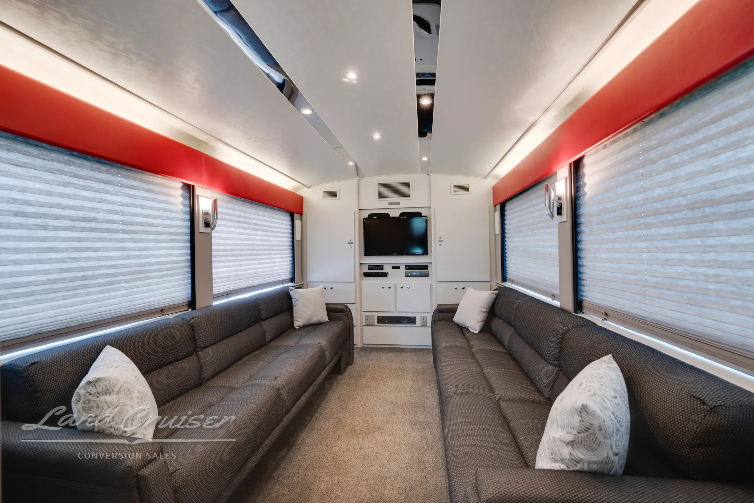 Rear-facing view of MCI Executive Coach interior showing twin gray sofas, entertainment console, and ambient ceiling lights