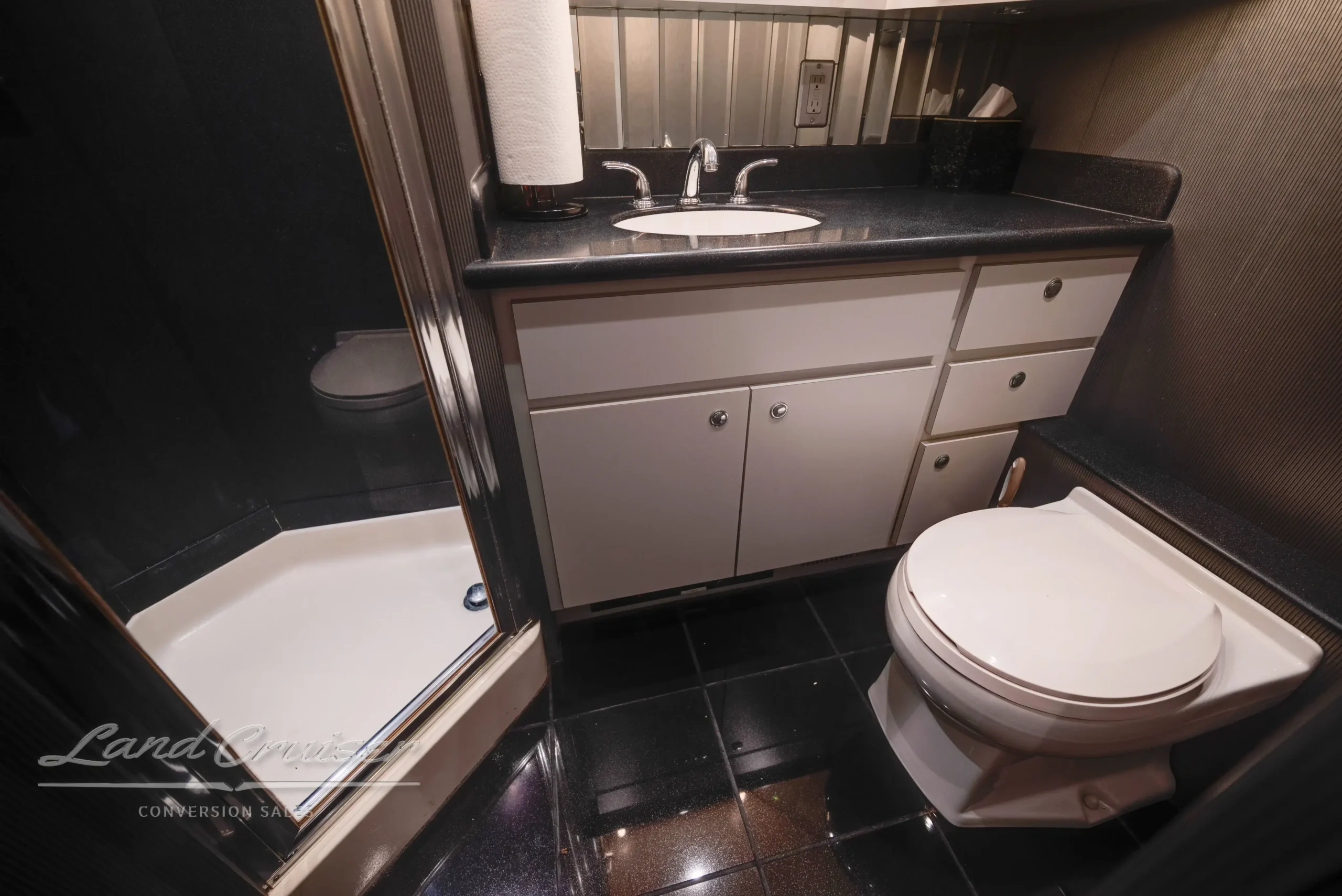 Bathroom in MCI 102-DL3 bus conversion with black countertops, under-sink cabinets, and ceramic toilet
