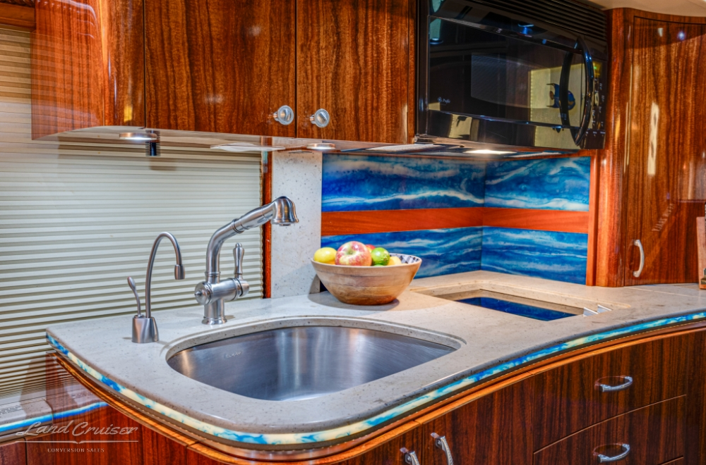 Kitchenette with a sink and microwave inside a prevost bus conversion for sale.