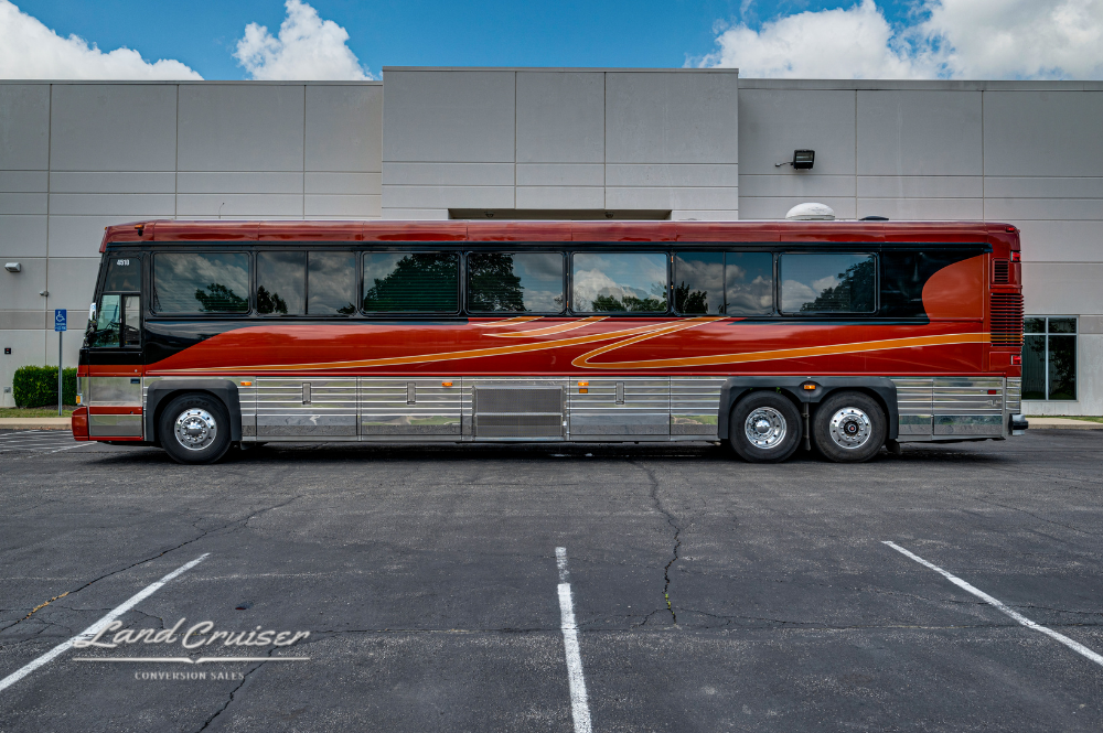 Driver side profile of Custom Coach 4510 parked beside commercial building under sunny sky