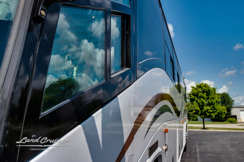 Reflections of sky and trees on passenger window of MCI motorhome