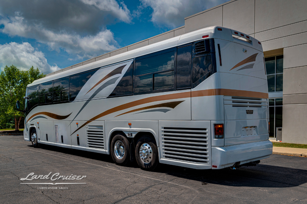 Passenger side view of MCI 102EL3 motorhome parked by building