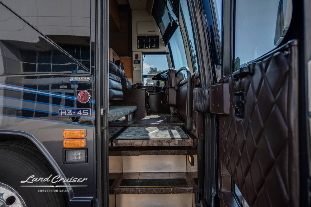 Entryway steps and front lounge view through open bus door, showcasing leather paneling and carpet.