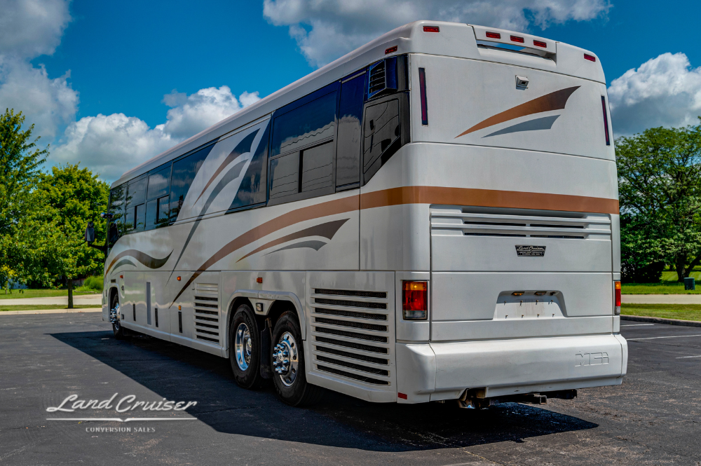 Rear corner view of white MCI 102EL3 with gold and brown stripes