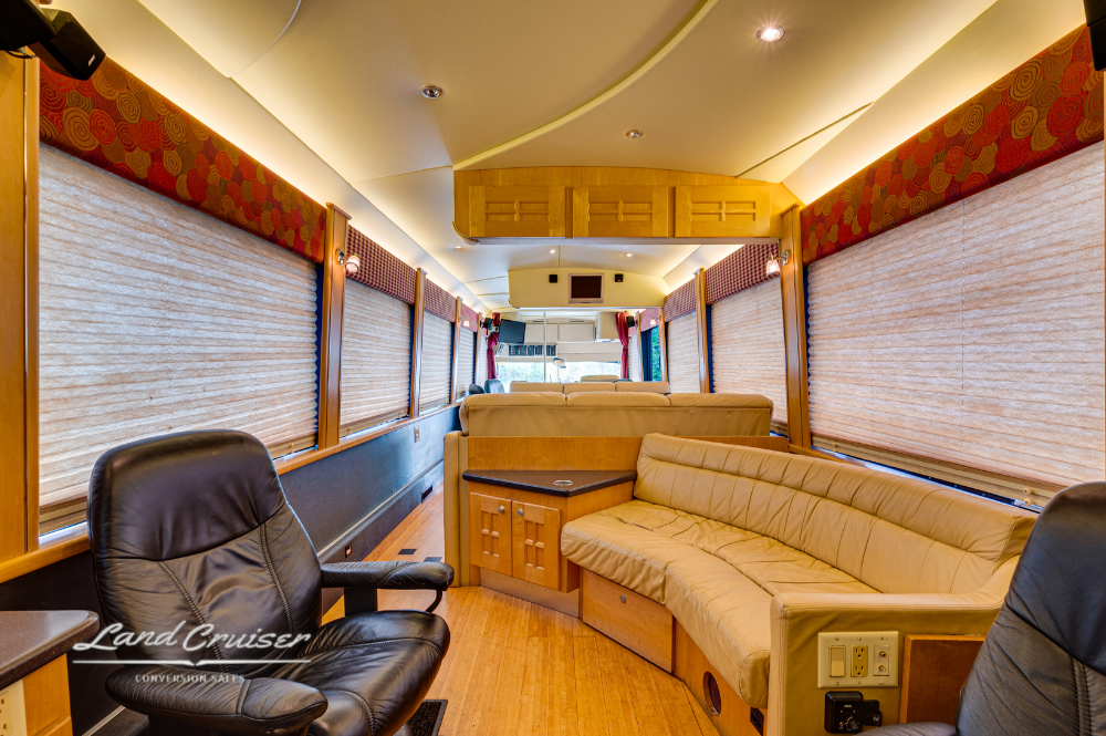 View of rear lounge with curved couch, black leather chair, and wood cabinetry under window blinds