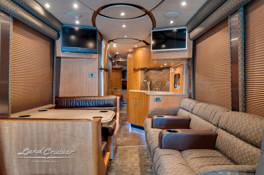 Dining and lounge area featuring two sofas, dining table, dual TVs, and wood cabinetry.