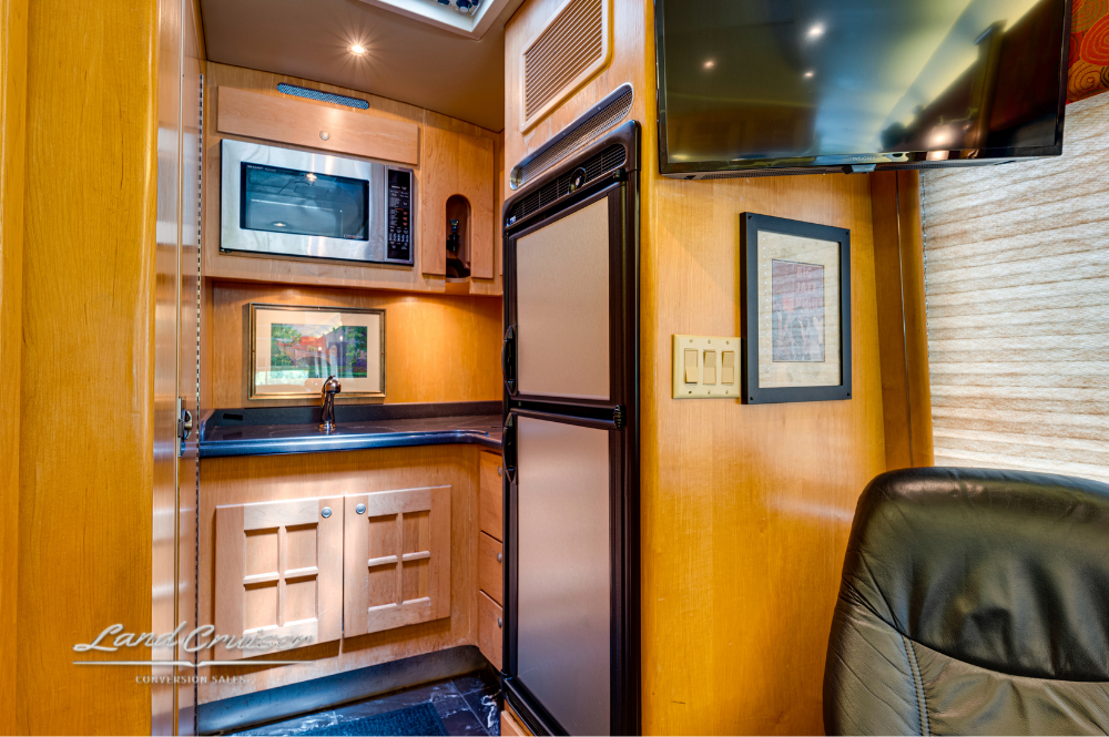 Galley kitchen featuring custom cabinetry, stainless microwave, fridge, and dark countertops
