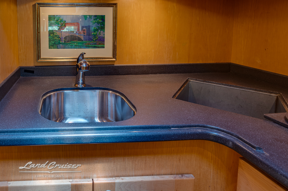 Corner kitchen counter with stainless steel sink, dark solid-surface countertop, and framed painting above