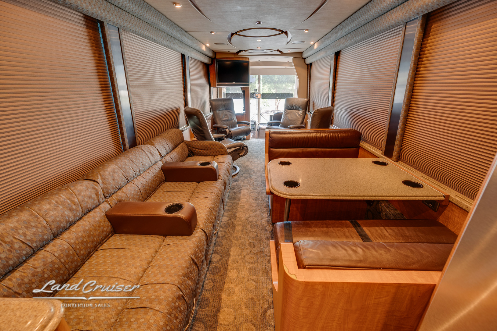 Dining and salon layout with dual sofas, wood-finish table, and full-length privacy shades.