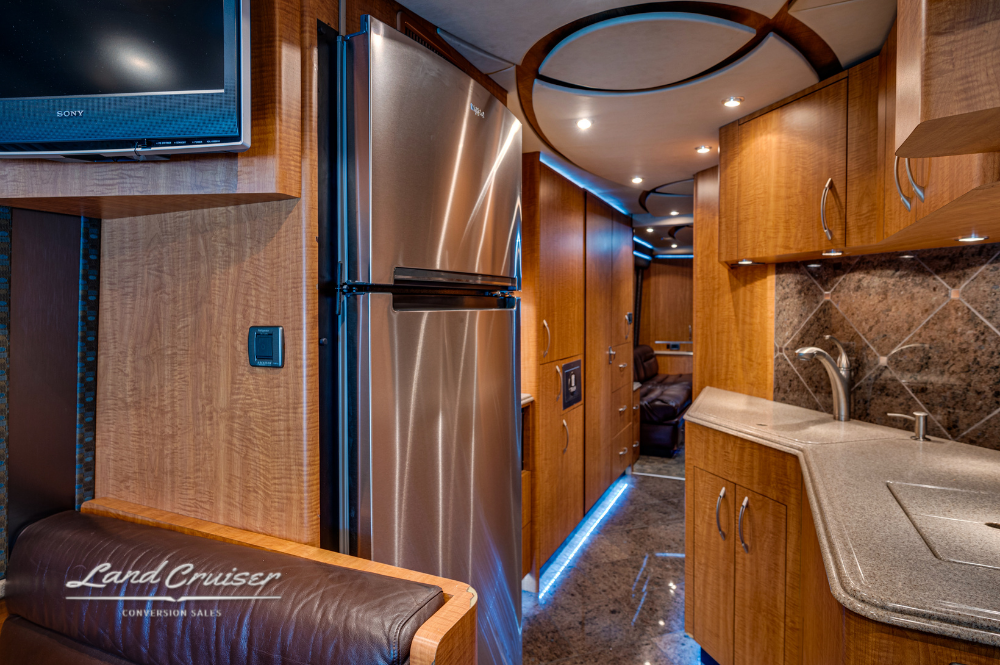 Galley view with residential refrigerator, mounted TV, and extended counter workspace.