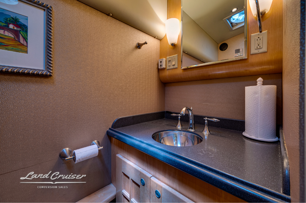 Vanity area with stainless steel sink, black countertop, paper towel holder, and wall mirror