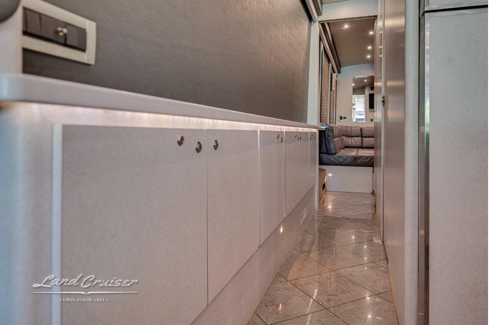 Cabinet-lined hallway leading to private lavatory and rear lounge in Prevost XLII conversion coach