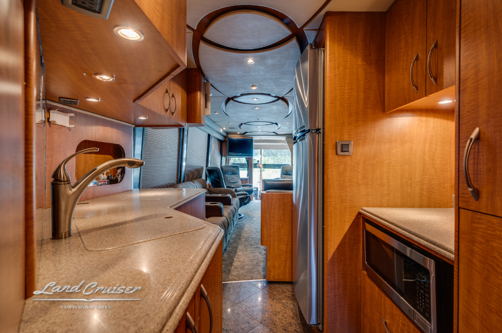 Galley view facing forward, featuring solid-surface countertops, sink, and overhead cabinetry.